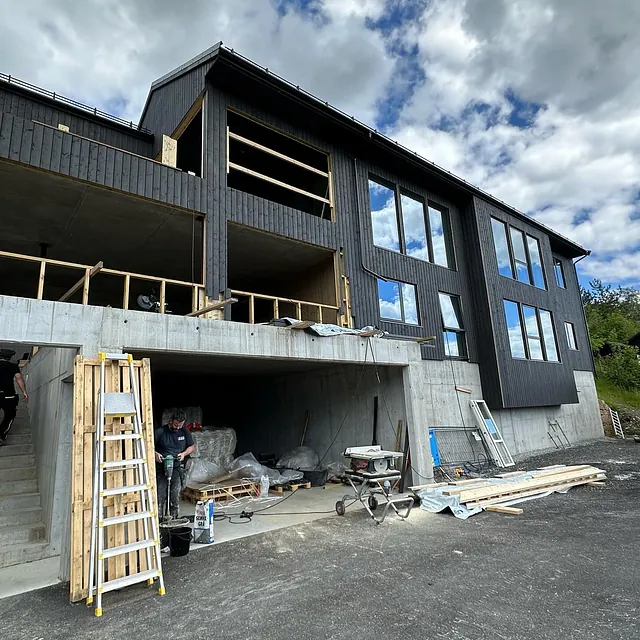 Stort hus eller flermannsbolig som har nesten fullført fasade. Vinduene som er satt inn reflekterer hvite skyer og blå himmel.