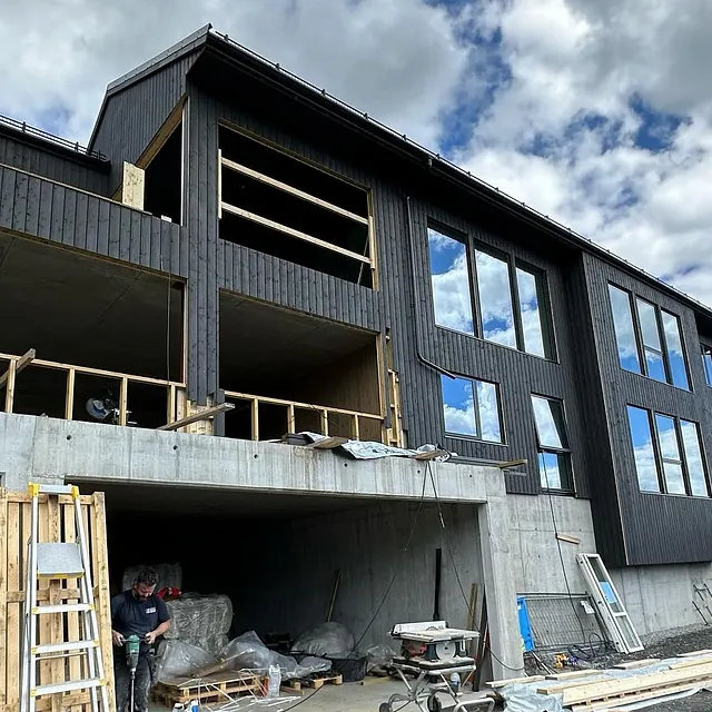 Stort hus eller flermannsbolig som har nesten fullført fasade. Vinduene som er satt inn reflekterer hvite skyer og blå himmel.